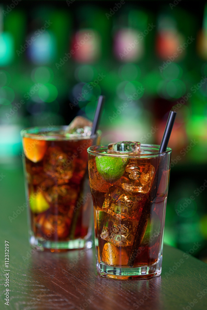 Cuba Libre is a famous Cuban cocktail. It is made of 2 oz light rum,juice of 1/2 limes,Coca-Cola. Shot on a bar in green light Cuba Libre is a famous Cuban cocktail. It is made of 2 oz light rum,juice of 1/2 limes,Coca-Cola. Shot on a bar in green light