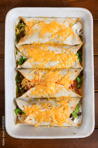 Mexican burittos in a baking dish. Shot from above over wooden background. Vertical shot photo