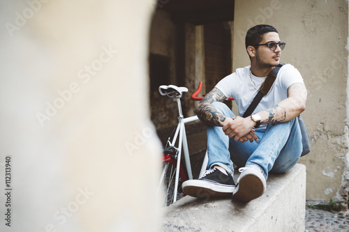 Young man with a bicycle sitting on wall