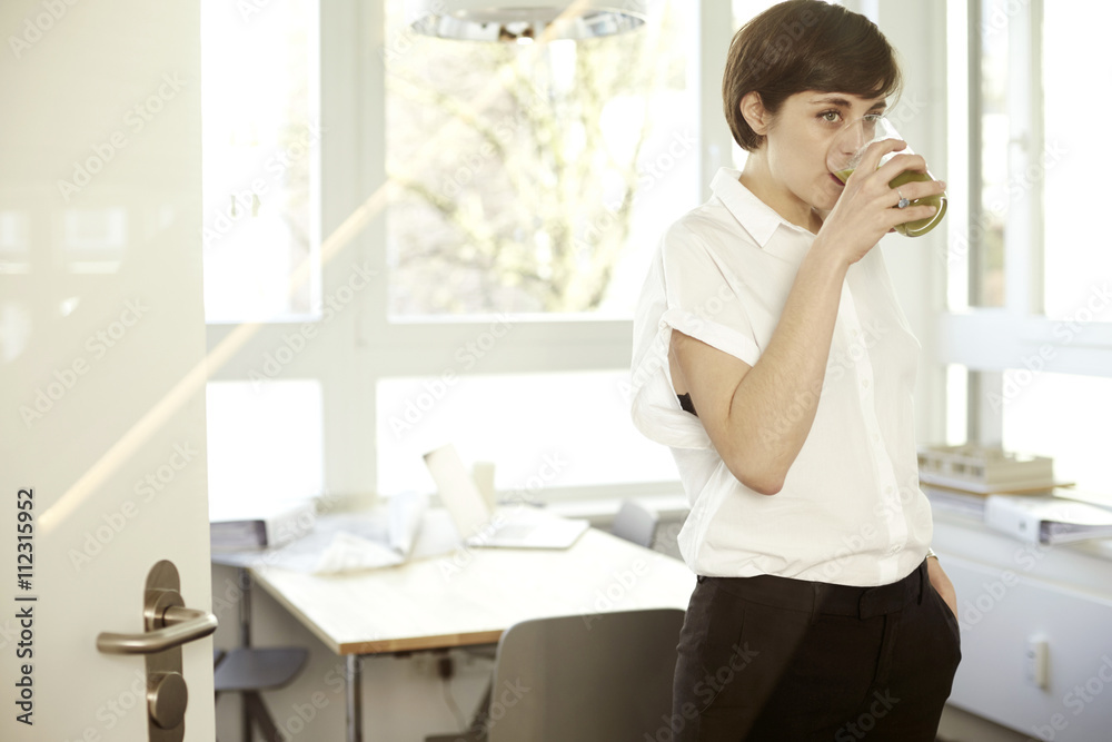 Woman drinking glass of green smoothie in an office Woman drinking glass of green smoothie in an office