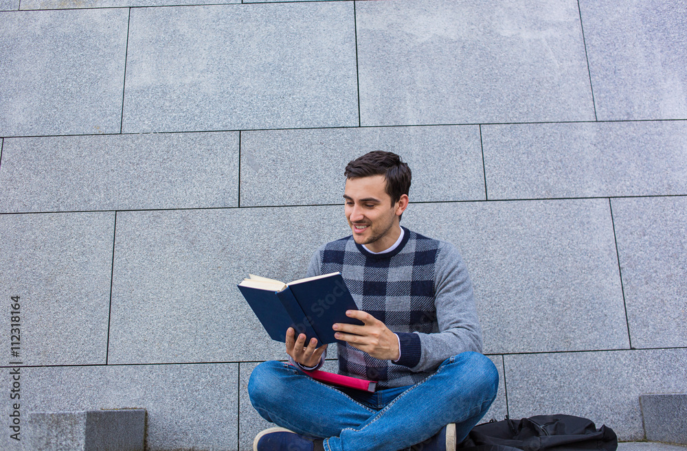 University.Smiling young student man holding and reading book in campus .Young smiling student outdoors Life style.City.Student.
