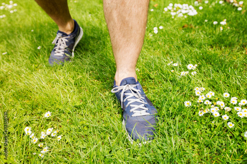Healthy active lifestyle man athlete with running shoes. Happy sporty runner man with blue sneakers on summer grass in city park getting ready for a fitness jog.
