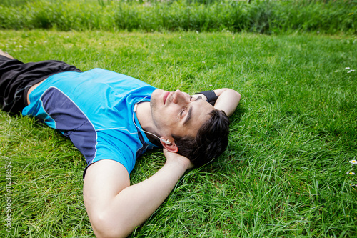 Sport fitness man relaxing listening to music after training outdoor in a city park . Young male athlete resting relaxing lying on grass after running and training exercise outside in summer. photo