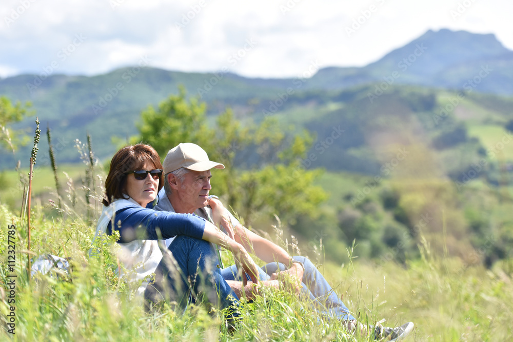 Senior hiking couple sitting in grass on journey