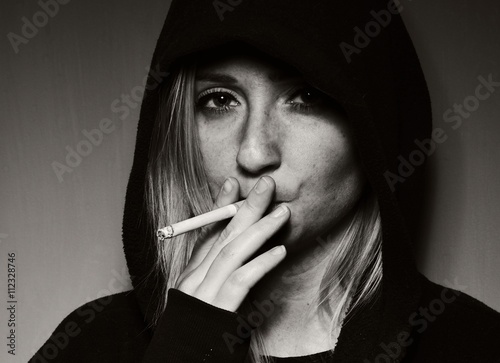 Obraz na płótnie Rebellious teenager in a hooded sweatshirt smoking a cigarette. w salonie