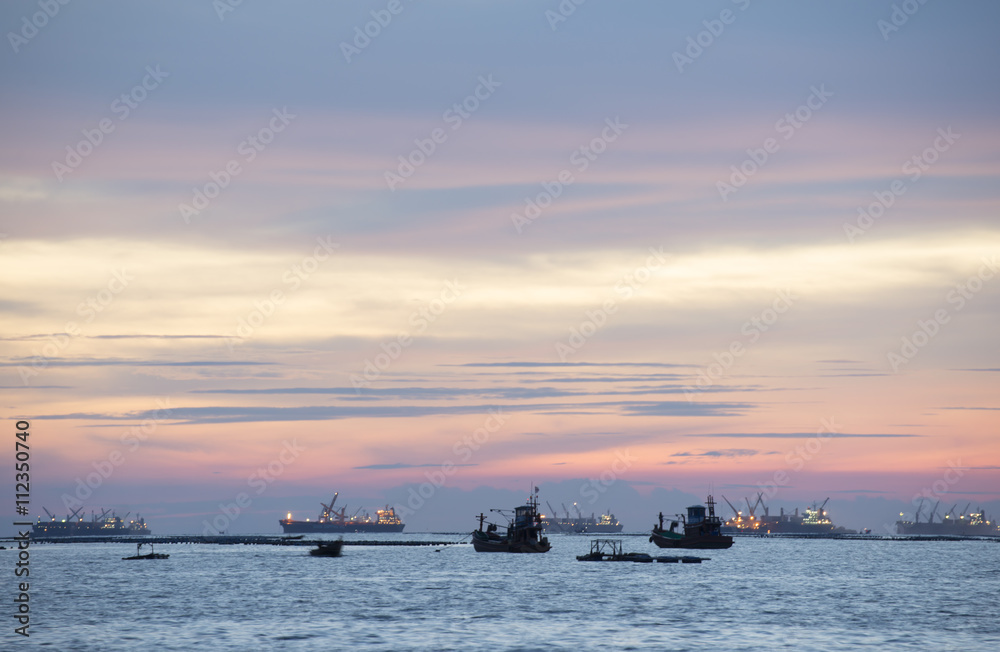 Twiling and sunset at the sea with fishing boat and cargo ship
