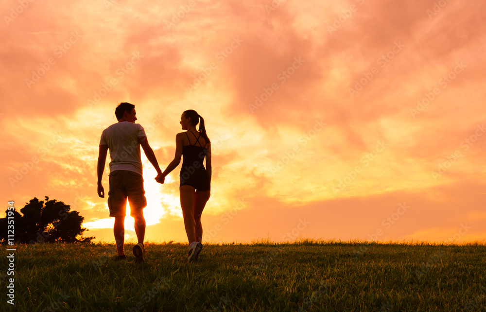 Couple holding hands and walking into the beautiful sunset. 