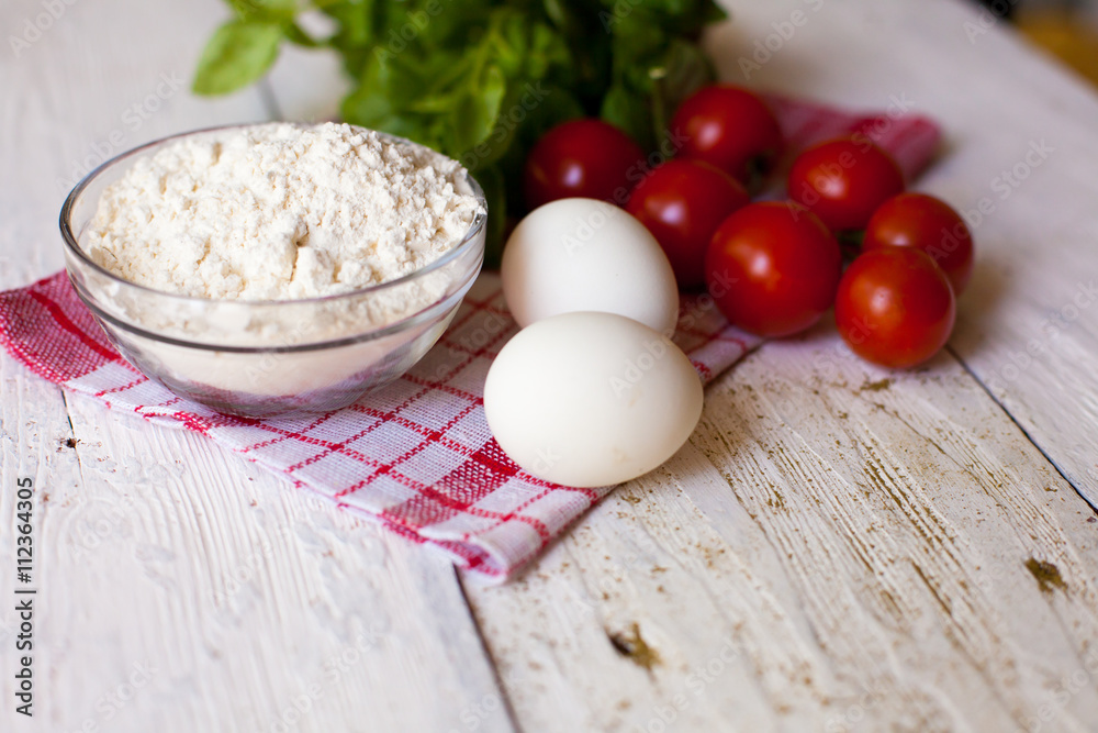 Cherry tomatoes,eggs, flour and basil on the table Cherry tomatoes,eggs, flour and basil on the table
