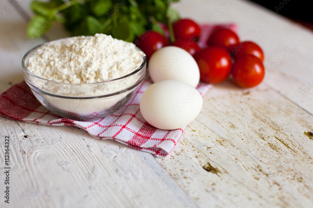Cherry tomatoes, eggs, flour and basil on the table Cherry tomatoes, eggs, flour and basil on the table