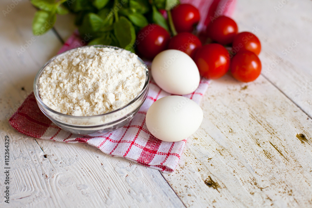 Cherry tomatoes, eggs, flour and basil on the table Cherry tomatoes, eggs, flour and basil on the table