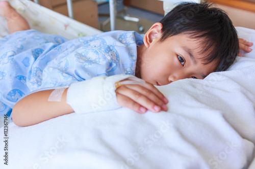 Asian boy lying on sickbed, saline intravenous (IV) on hand.