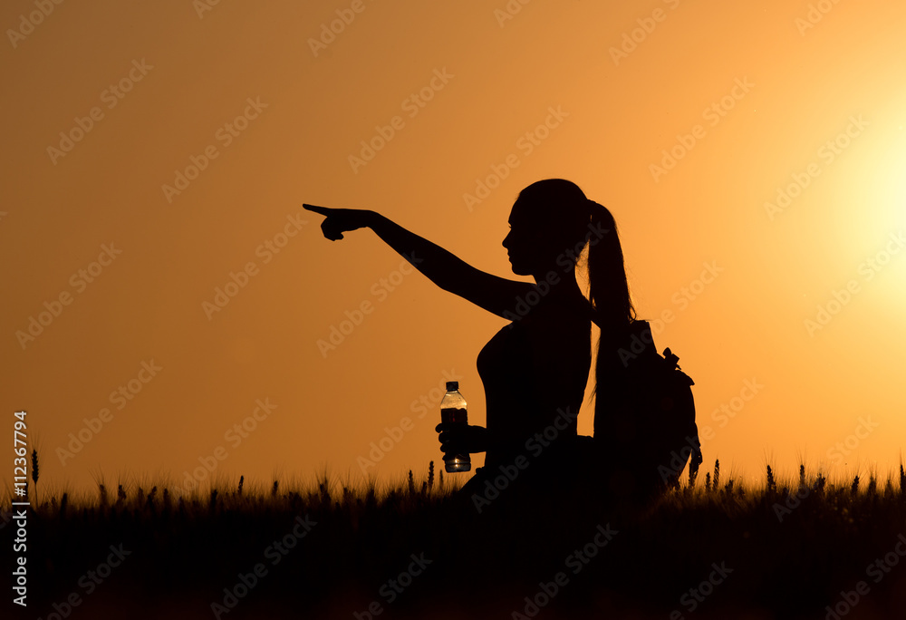 Woman hiker standing in wheat field at sunset