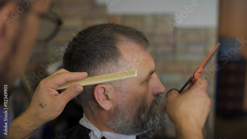 hairdresser cuts hair with scissors on crown client in professional hairdressing salon. The gray-haired man in the age of the client in the chair.