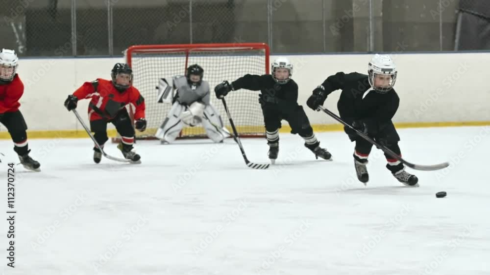 Four little boys playing professional hockey: one of them handling puck and three players skating behind him in slow motion; goaltender standing in the background. Shot on Sony Nex 700