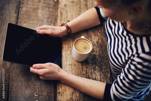 Close-up of female hands holding digital computer sitting at wooden table with cup of macchiato. Concept of business, mobility and lifestyle. 