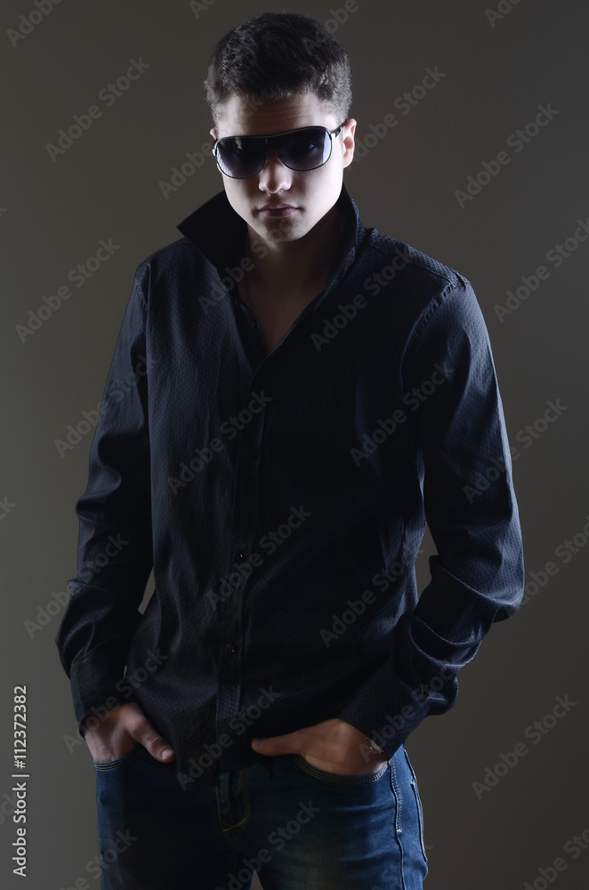 Fashion portrait of young man in black shirt poses over wall Fashion portrait of young man in black shirt poses over wall