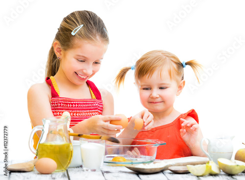 two smiling little sisters cooking on a white background