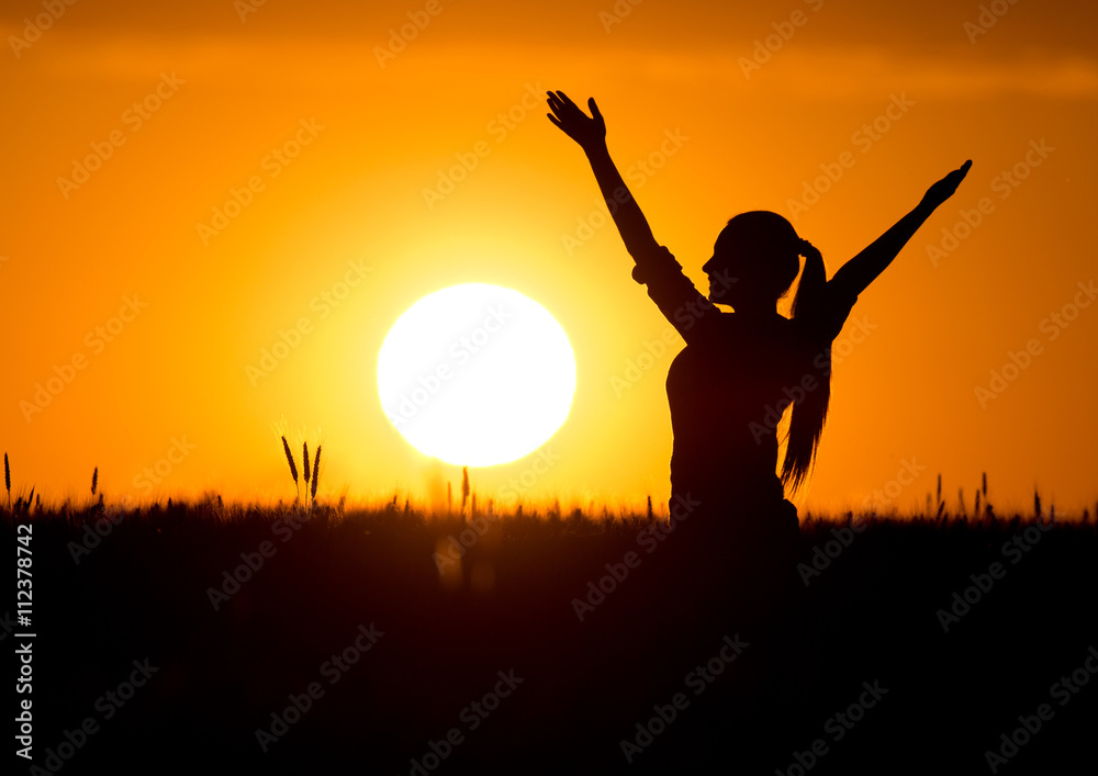 Silhouette of girl with raised hands at sunset