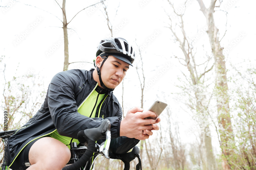 Man in cycling helmet with bicycle using smartphone in park Man in cycling helmet with bicycle using smartphone in park