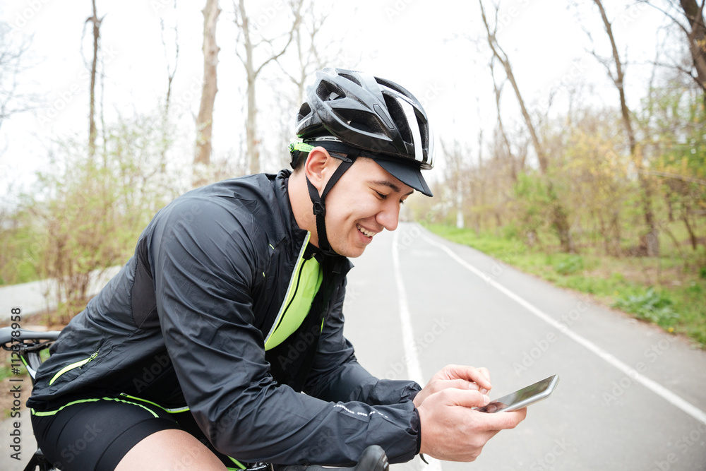 Cheerful young man with bicycle using mobile phone