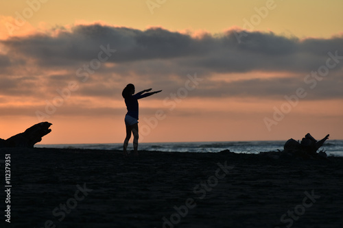Female doing exercise on sea shore in weak light at dusk.