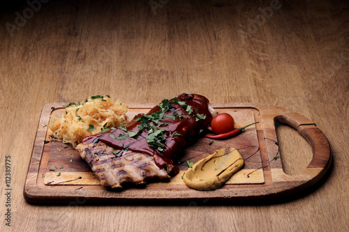 Port steak with red sauce with braised cabbage, fresh cherry tometoes and mustard served on wooden board on rustic wooden counter photo