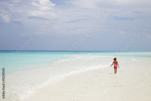Young girl walking on an empty white sand beach, back view