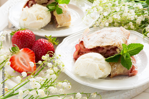 Homemade strudel with strawberries decorated ice-cream and mint leaves on white wooden background