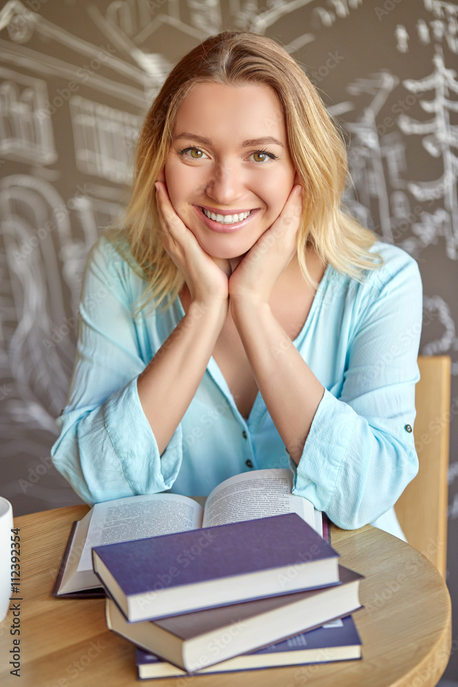 Beautiful young woman sitting at the table with open book at the cafe. Holding herself for face. Beautiful young woman sitting at the table with open book at the cafe. Holding herself for face.