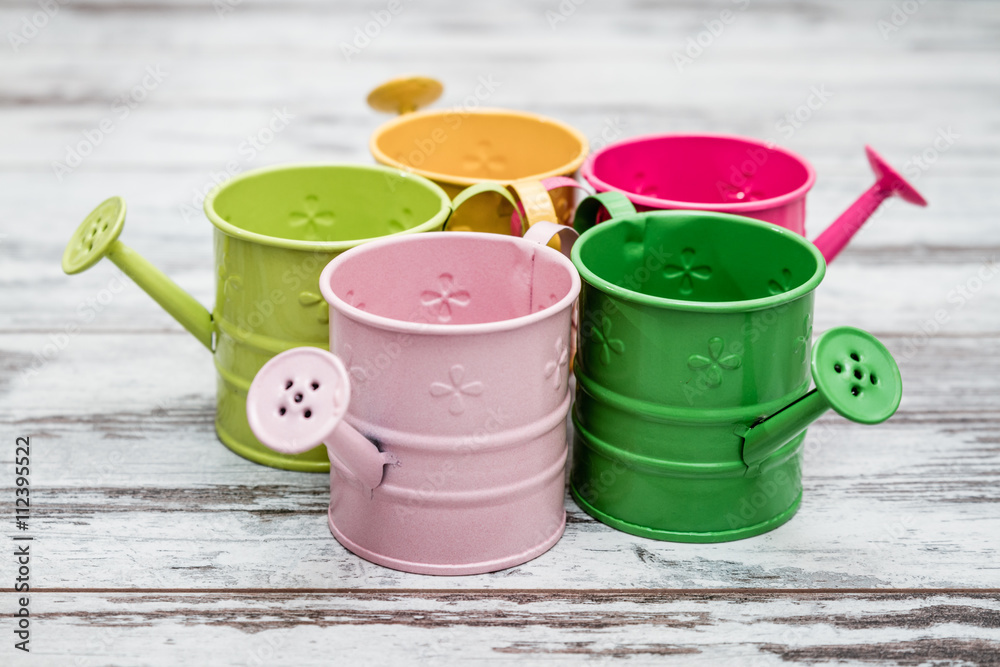 Simple Colorful Metallic Watering Cans on White Wooden Background