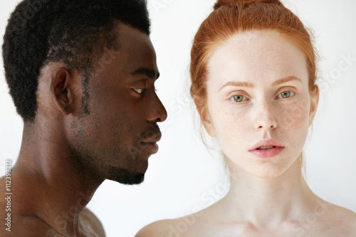 Profile of African male looking at his beautiful Caucasian girlfriend or wife with loving and caring expression on his face, while she is looking at the camera. Interracial multi-ethnic relationships
