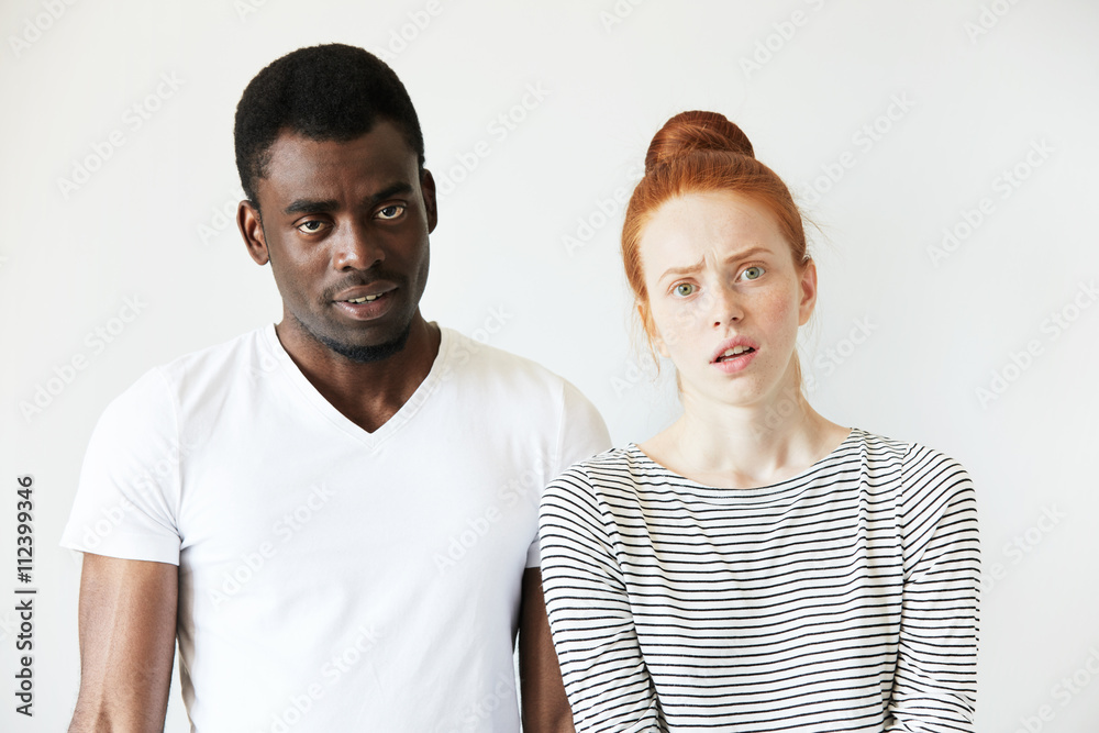 African man wearing white T-shirt standing next to his Caucasian girlfriend in sailor shirt, looking at the camera with disgusted and annoyed expression, quarrelling or breaking up. Human relations African man wearing white T-shirt standing next to his Caucasian girlfriend in sailor shirt, looking at the camera with disgusted and annoyed expression, quarrelling or breaking up. Human relations