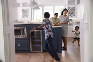 Parents Prepare Food As Children Play In Kitchen