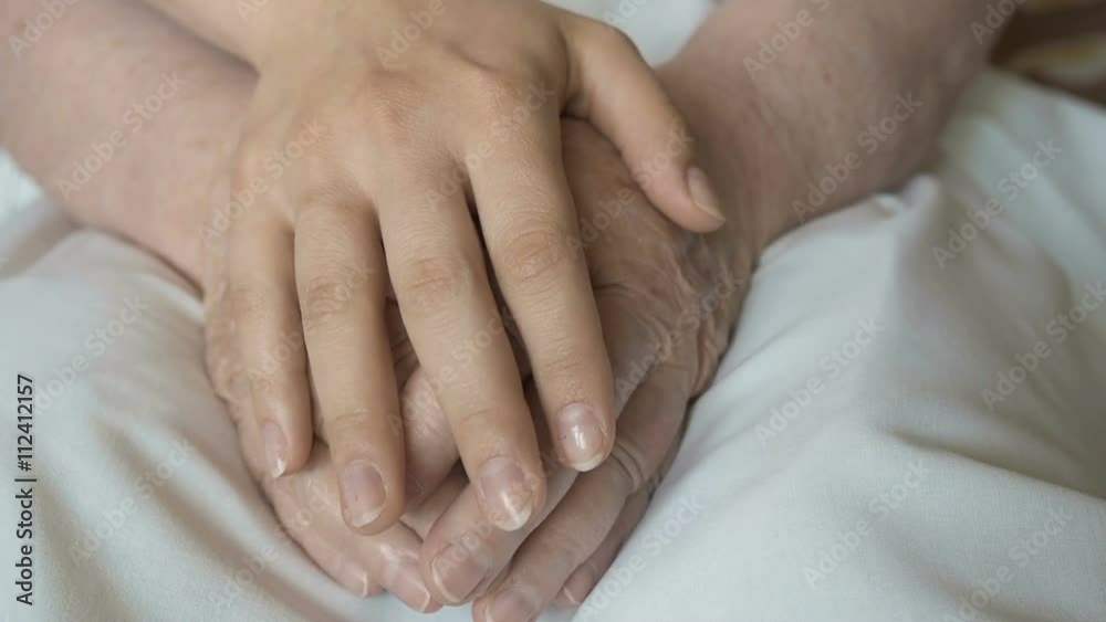 A young female hands comforting an elderly pair of hands of old women A young female hands comforting an elderly pair of hands of old women