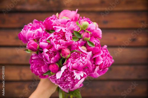 Fototapeta Naklejka Na Ścianę i Meble -  Beautiful bouquet of dark pink peonies in woman hands on a wooden background. Bunch of flowers in hands. Stripes. Summer time.