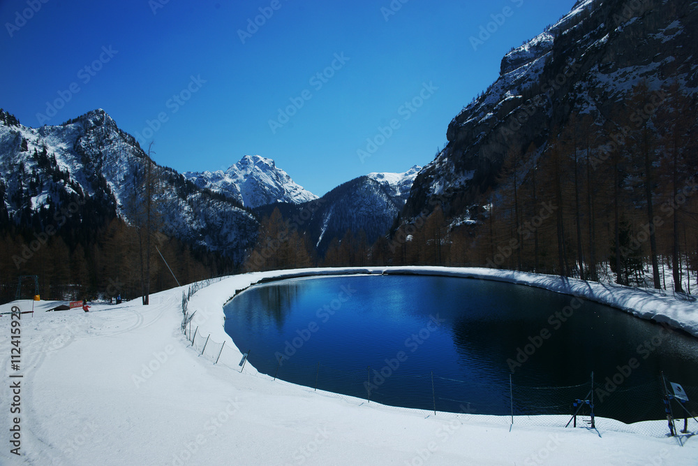 View on small lake and mountain peaks against blue sky on a sunny winter day