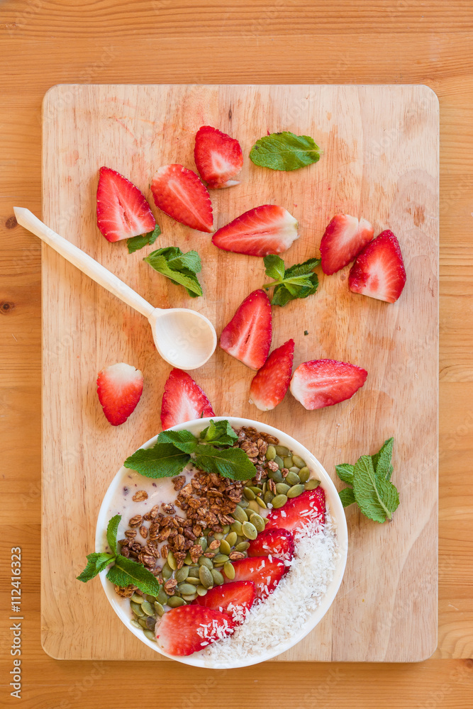 Breakfast berry smoothie bowl topped with strawberry, pumpkin seeds, coconut, muesli and fresh mint. Strawberry banana smoothie bowl. healthy breakfast or snack, wooden tableware. Breakfast berry smoothie bowl topped with strawberry, pumpkin seeds, coconut, muesli and fresh mint. Strawberry banana smoothie bowl. healthy breakfast or snack, wooden tableware.