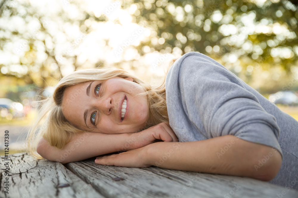 Portrait of young blond woman lying on the old wooden table and enjoying sunny day. Walking in the park. Smiling girl outdoor. Portrait of young blond woman lying on the old wooden table and enjoying sunny day. Walking in the park. Smiling girl outdoor.