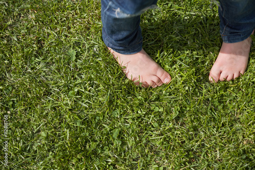Top view on kid's bare feet on the green grass. Little boy standing on the grass in the park on a sunny day. Child's bare feet.