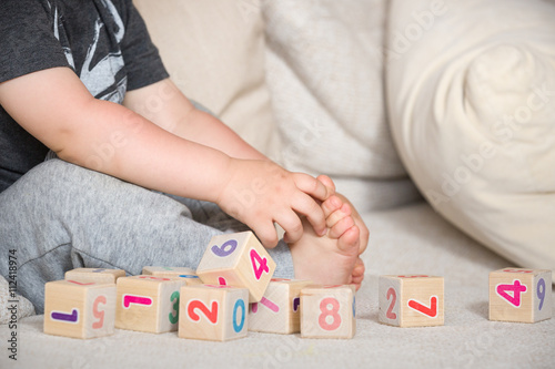 Child playing with wooden cubes with numbers. Toddler learning numbers. Hand of a child taking toys. Boy on the sofa at home, indoors. Education and learning concept.