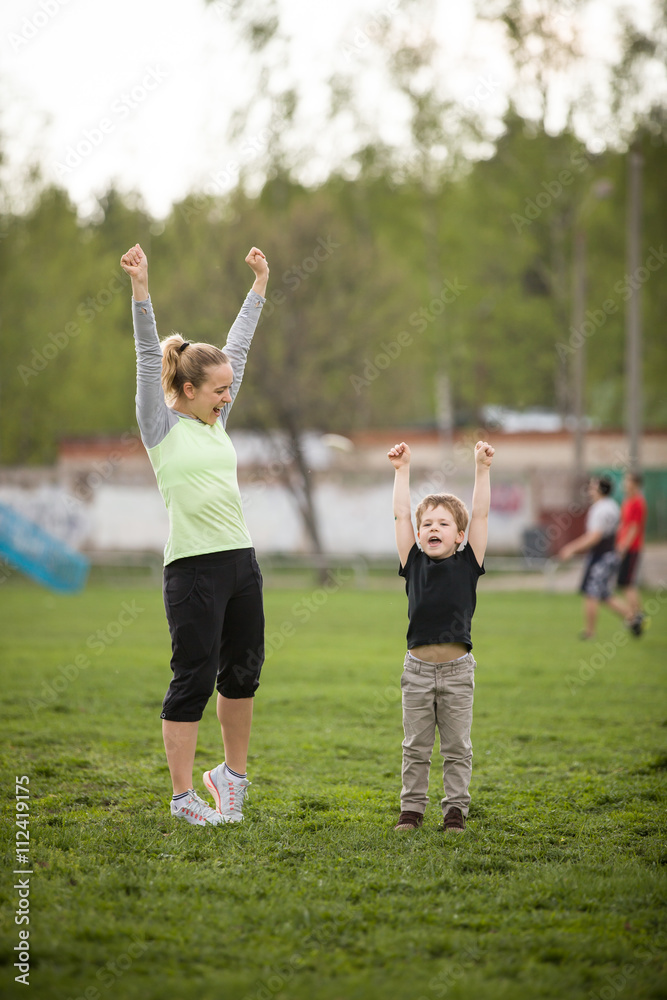 Obraz premium Happy mother and son on the stadium enjoying their sport activities. Family doing exercises outdoors and greeting winners. Fitness, healthy lifestyle, together concept.