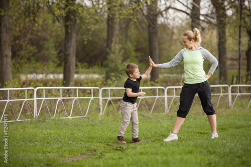 Happy son and mother are doing exercises in the summer park. on the stadium, outdoor. Sport activities with children. Healthy lifestyle. Fitness exercises. Young mother and son are stretching together
