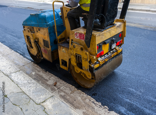 Light vibration roller compactor at asphalt pavement works for road repairing..On the frame are visible signs of job security: "Keep clear of the operating range of the machine"