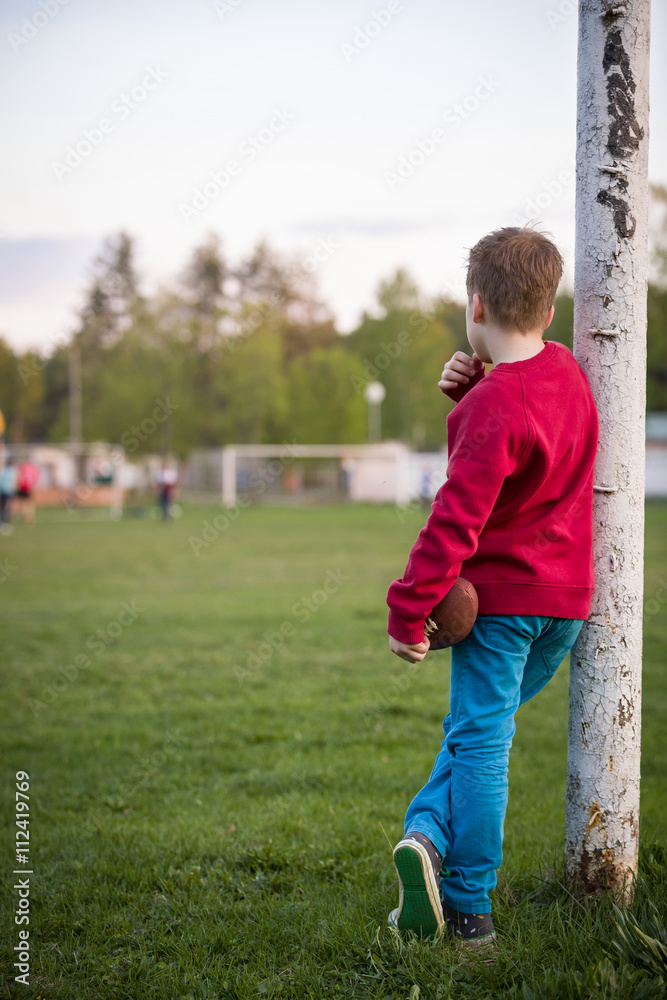 Little soccer player standing in the goalposts defending the the line and ready to throw a football. Cute kid boy standing as goalkeeper on a sportsfield on a sunny day. Sport activities for children