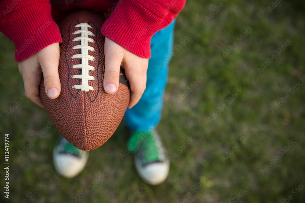 Top view on hands of little kid boy holding football on the stadium on