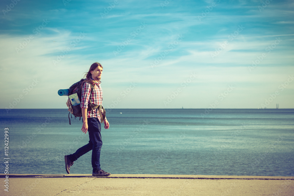Man hiker with backpack tramping by seaside Man hiker with backpack tramping by seaside