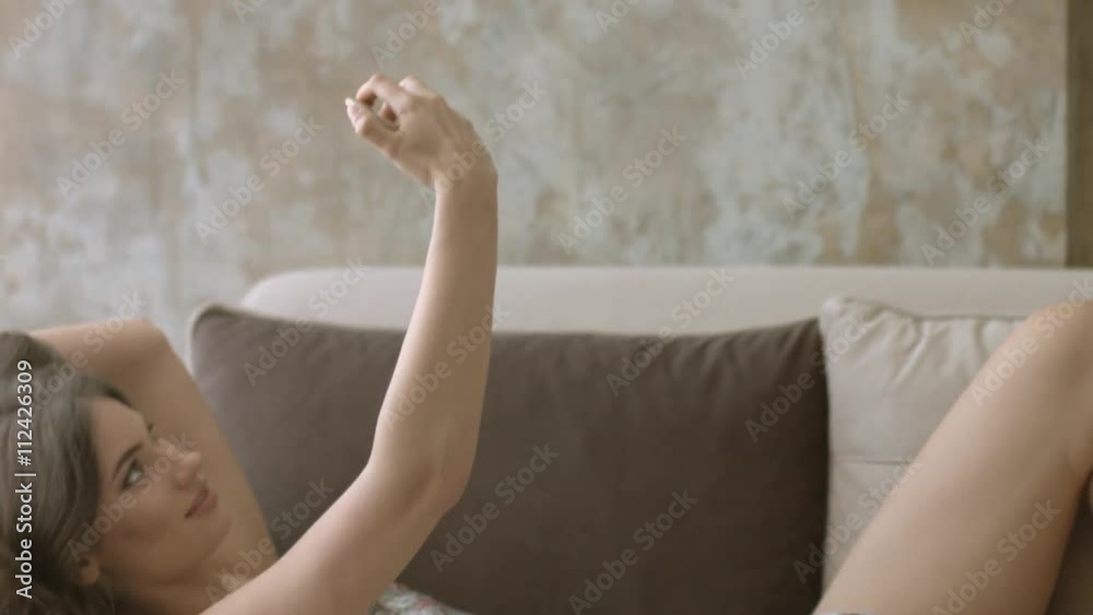 Charming brunette in nightie lying on the couch and doing selfie on the phone Charming brunette in nightie lying on the couch and doing selfie on the phone