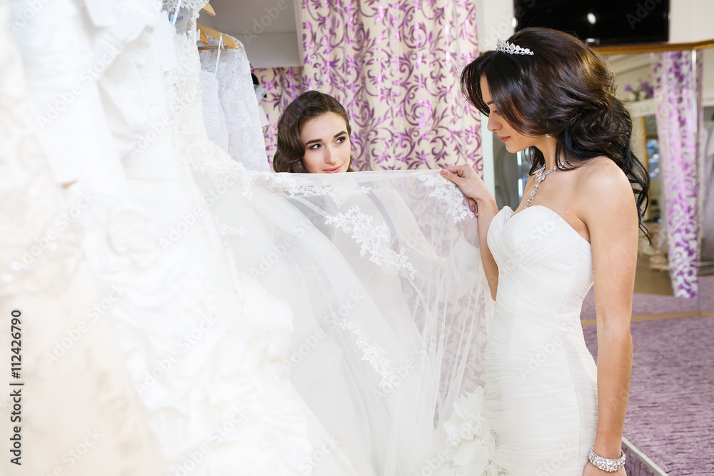 Female trying on wedding dress in a shop with women assistant.