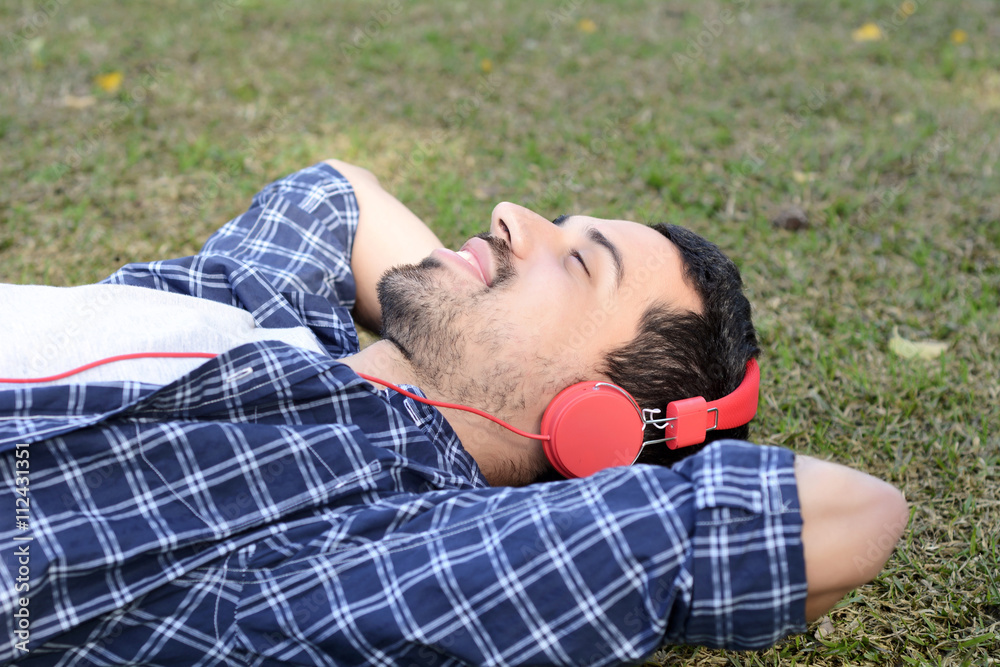 Young man listening to music with headphones in park.