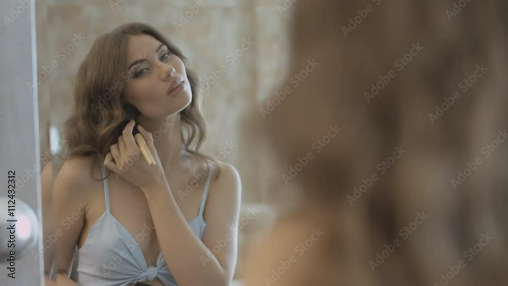 Beautiful girl standing before the mirror and applying the powder on the face using a brush Beautiful girl standing before the mirror and applying the powder on the face using a brush